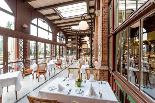 un ristorante con tavoli e sedie bianchi e finestre di Dorint Herrenkrug Parkhotel Magdeburg a Magdeburgo