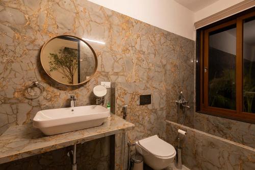a bathroom with a sink and a toilet and a mirror at StayVista at Sunset on the Lake - Infinity Lakeview Swimming Pool with Contemporary Interiors & Lavish Amenities in Igatpuri