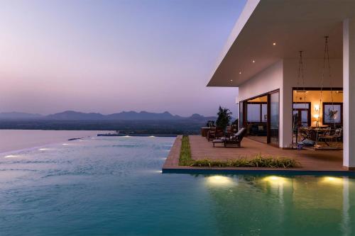 a house with a swimming pool next to a body of water at StayVista at Sunset on the Lake - Infinity Lakeview Swimming Pool with Contemporary Interiors & Lavish Amenities in Igatpuri