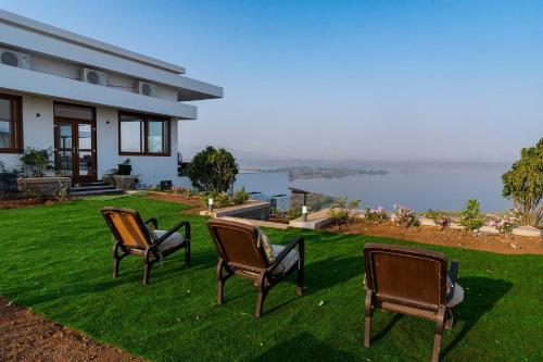 three chairs sitting on a lawn in front of a house at StayVista at Sunset on the Lake - Infinity Lakeview Swimming Pool with Contemporary Interiors & Lavish Amenities in Igatpuri