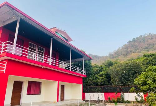 a red building with a balcony in front of a mountain at Kanva Farms in Kotdwāra