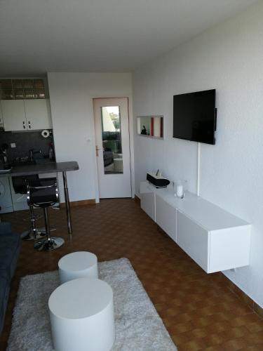Il comprend un salon doté d'une armoire blanche et d'une télévision à écran plat. dans l'établissement Naturisme appartement heliopolis face à la plage avec vue mer, au Cap d'Agde