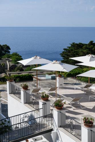 a patio with white umbrellas and chairs and the ocean at La Residenza Capri in Capri