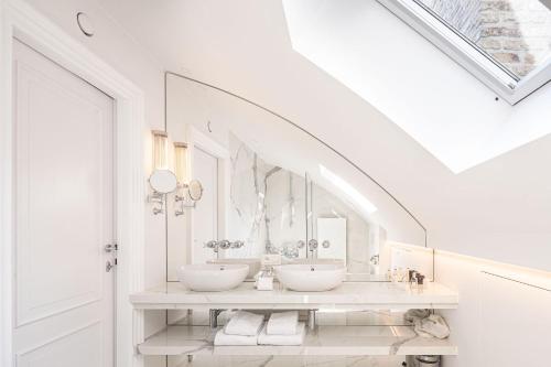 a white bathroom with two sinks and mirrors at De Tuilerieën - Small Luxury Hotels of the World in Bruges