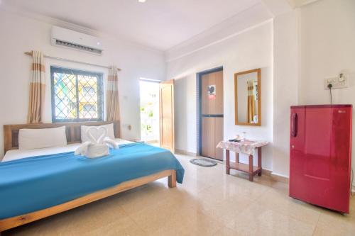 um quarto com uma cama azul e um frigorífico vermelho em Baga Beach Rosy Inn em Baga