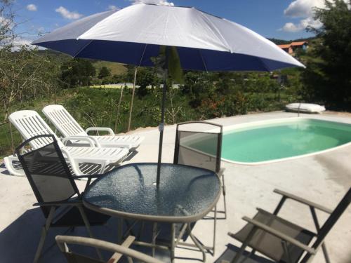 a table and chairs with an umbrella next to a pool at Recanto das Acácias in Guararema