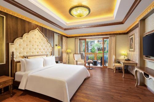 um quarto com uma grande cama branca e uma televisão em Kaldan Samudhra Palace em Mahabalipuram