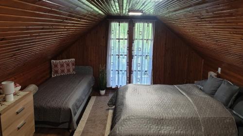 a attic bedroom with two beds and a window at FÜGE-FA-HÁZ VÁSÁROSNAMÉNY - GERGELYIUGORNYA in Vásárosnamény