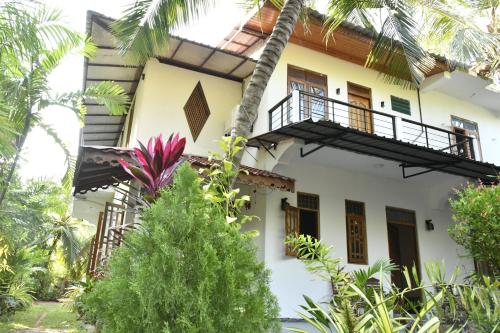 ein weißes Haus mit einem Balkon und Palmen in der Unterkunft Pearl Bungalow Trincomalee in Trincomalee