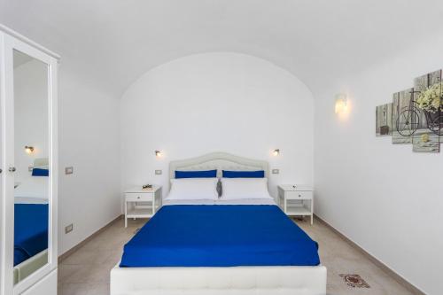 a white bedroom with a blue bed and a mirror at Villa Salice in Amalfi