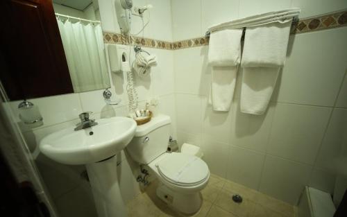 a white bathroom with a toilet and a sink at Hotel Los Jardines in Santiago de los Caballeros