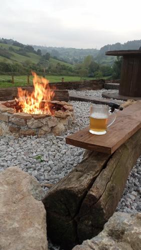 a glass of beer sitting on a wooden table next to a fire at Glamping Quintana in Gijón