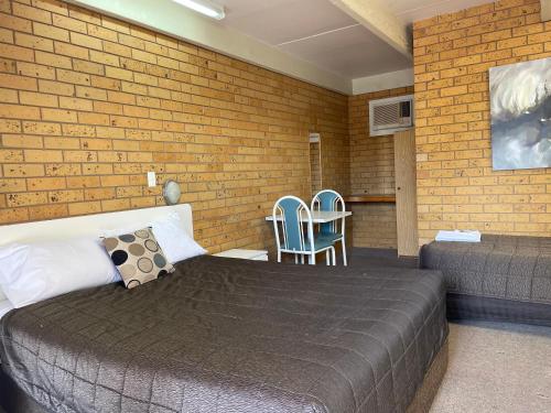 a bedroom with a bed and chairs and a brick wall at Citrus Motel in Griffith