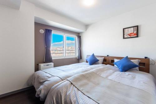 a bedroom with two beds with blue pillows and a window at GLOW in Otaru