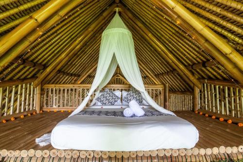 a large bed in a thatched room at Balikayanas Bamboo House - Miggiell House in Karangasem