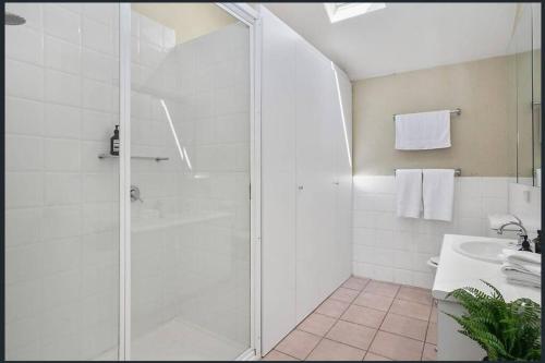 La salle de bains blanche est pourvue d'une douche et d'un lavabo. dans l'établissement Lonnie Beach View Apartment, à Point Lonsdale