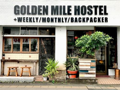 a white building with a sign that reads golden mile hospitalweekly monthly back packeper at ゴールデンマイルホステル３Ｆ完全個室Ｂタイプ in Amami