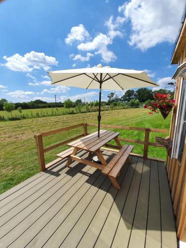 a wooden picnic table with an umbrella on a deck at Dartmoor Reach Alpaca Farm Heated Cabins 5 mins drive to Dartmoor in Bovey Tracey