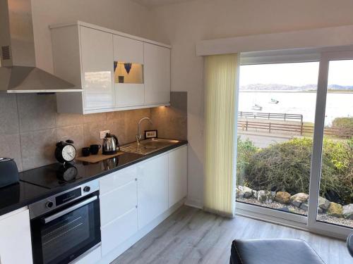 a kitchen with white cabinets and a large window at Ards House Self catering apartment with sea views in Oban