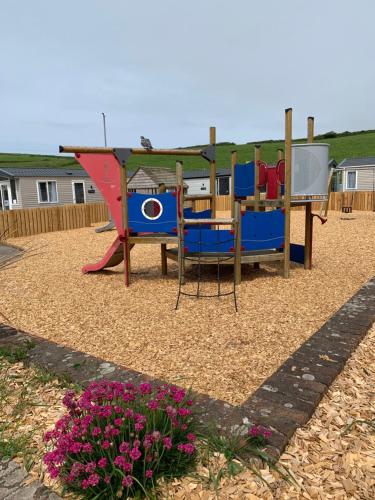a park with a playground with a slide and flowers at Newquay Bay Resort 63 in Newquay Bay Resort