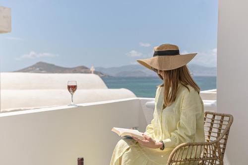 a woman sitting in a chair reading a book and a glass of wine at Flèria Seaview Suites in Naxos Chora
