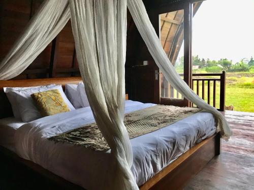 1 dormitorio con 1 cama con cortinas en Kubu Bakas Guest House - CHSE Certified, en Banjarangkan
