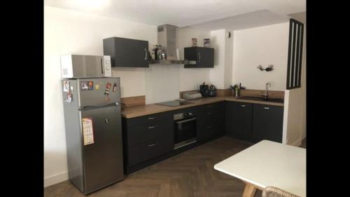 une cuisine avec des armoires noires et un réfrigérateur en acier inoxydable dans l'établissement Charmant T2 de 45m2 - parking privé - terrasse- linge inclu- Proche Vannes, à Saint-Avé