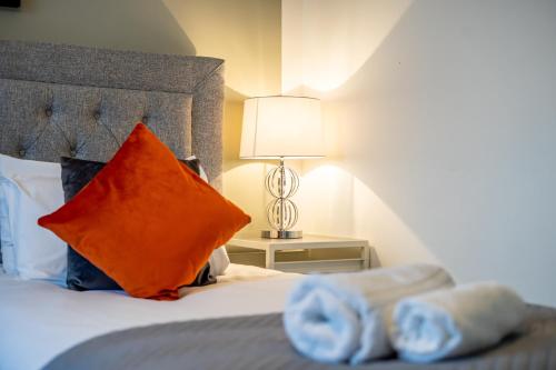 a bedroom with a bed with an orange pillow and a lamp at Inspiration by Olauda SA - 3 Bed House with Free Parking in Swindon