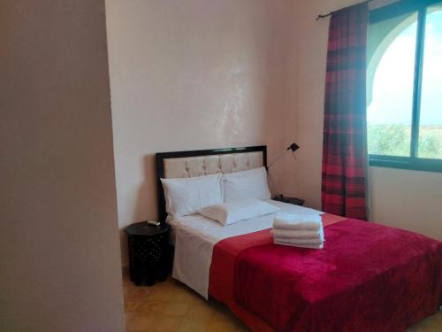 1 dormitorio con 1 cama con manta roja y ventana en Amizmiz Villa, en Marrakech