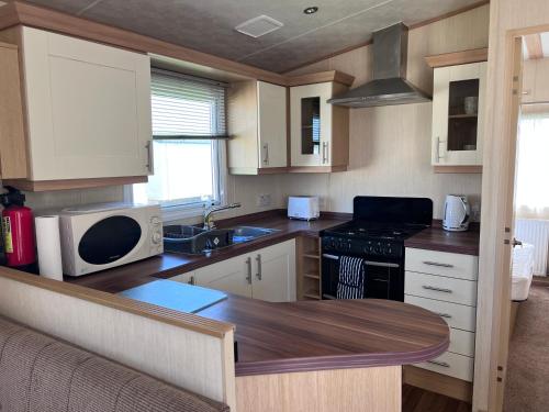 a small kitchen with a sink and a microwave at PG174 Golden Palm Resort 8 Berth Caravan With Decking in Chapel Saint Leonards