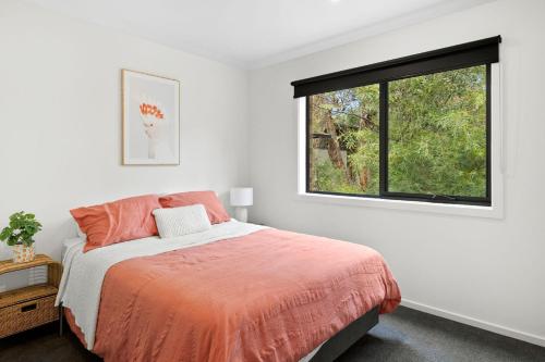 a bedroom with a bed with an orange blanket and a window at Chatleys in Aireys Inlet