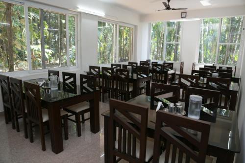 a dining room with tables and chairs and windows at Hosamane Farm Inn in Sringeri