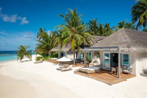 a resort on a beach with chairs and palm trees at Baglioni Resort Maldives - Luxury All Inclusive in Dhaalu Atoll