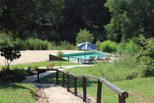 a swimming pool with an umbrella and chairs and a bench at Lions Rock Rapids - Lodge in Hazyview