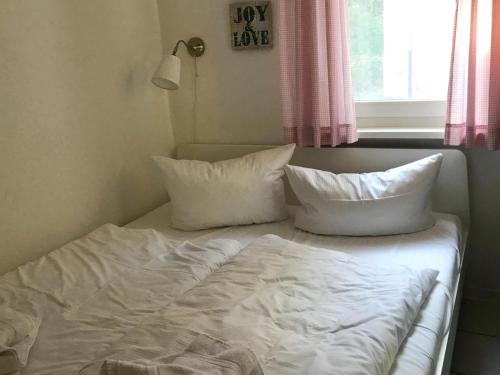 Cama con sábanas blancas y almohadas junto a una ventana en Bungalow 68 am Waldrand, en Glowe