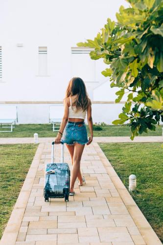 a woman walking with a suitcase on a sidewalk at B&B Domus Terra Mare in Torre San Giovanni Ugento