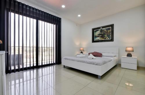 a white bedroom with a bed and a large window at Sea view apartment in Birżebbuġa