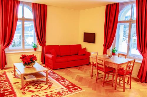 a living room with a red couch and a table at Maloja Palace Suites CO2-Neutral in Maloja