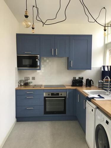 a kitchen with blue cabinets and a washer and dryer at The Store, harbour holiday cottage in Port Seton