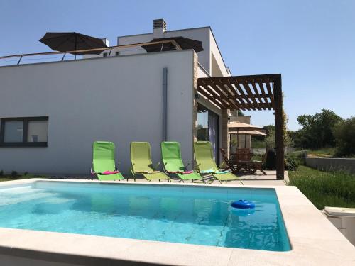 a swimming pool with green chairs and a house at Villa Rosa dei Venti - Peroj - Amazing sea view in Peroj