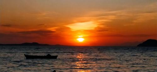 a boat in the ocean with a sunset at L&M Housing Apartamentos y casa in Búzios