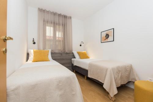 two beds in a room with white walls and yellow pillows at Apartments Agava in Rabac