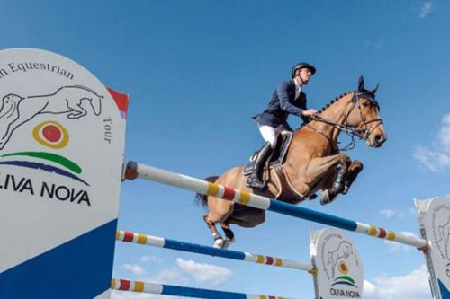 eine Person, die auf einem Pferd reitet und über ein Hindernis springt in der Unterkunft Blue Oliva Nova MET & Golf in Oliva