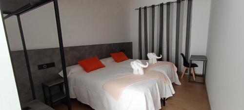 a bedroom with two beds with white sheets and orange pillows at Pensión Mar in Portomarin
