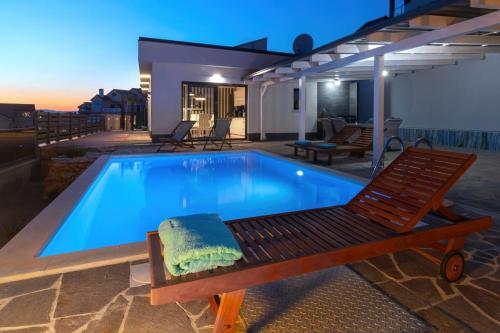 a swimming pool with a bench and a chair next to it at Villa Belissima Vista Mare in Selce