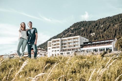 una pareja de pie en una colina frente a un edificio en Seehotel Panorama Relax, en Resia