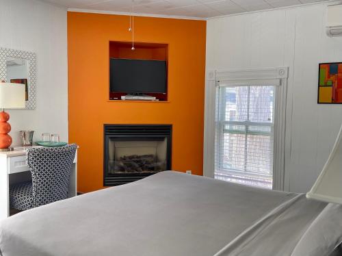 a bedroom with an orange wall with a tv and a fireplace at Somerset House Inn in Provincetown