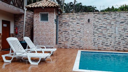 two chairs and a swimming pool in front of a brick wall at Solar Maresias Flats in Maresias