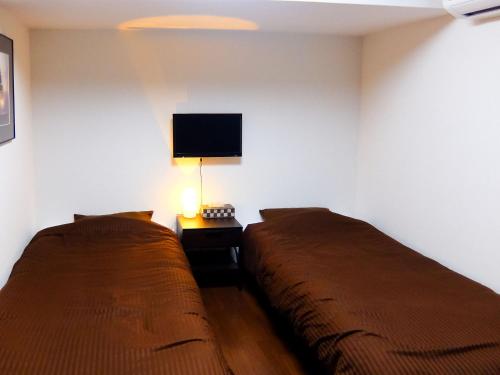two beds in a room with a tv on the wall at Guesthouse Bell Fushimi in Kyoto
