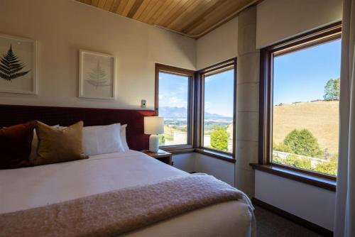 a bedroom with a bed and two large windows at Cabot Lodge - Fiordland National Park in Manapouri